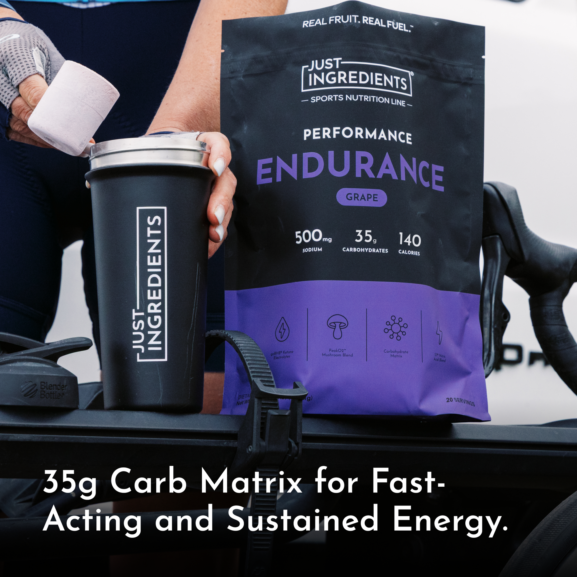 Black pouch of grape-flavored endurance drink with 35g carbohydrates and 500mg sodium, held next to matching black tumbler.