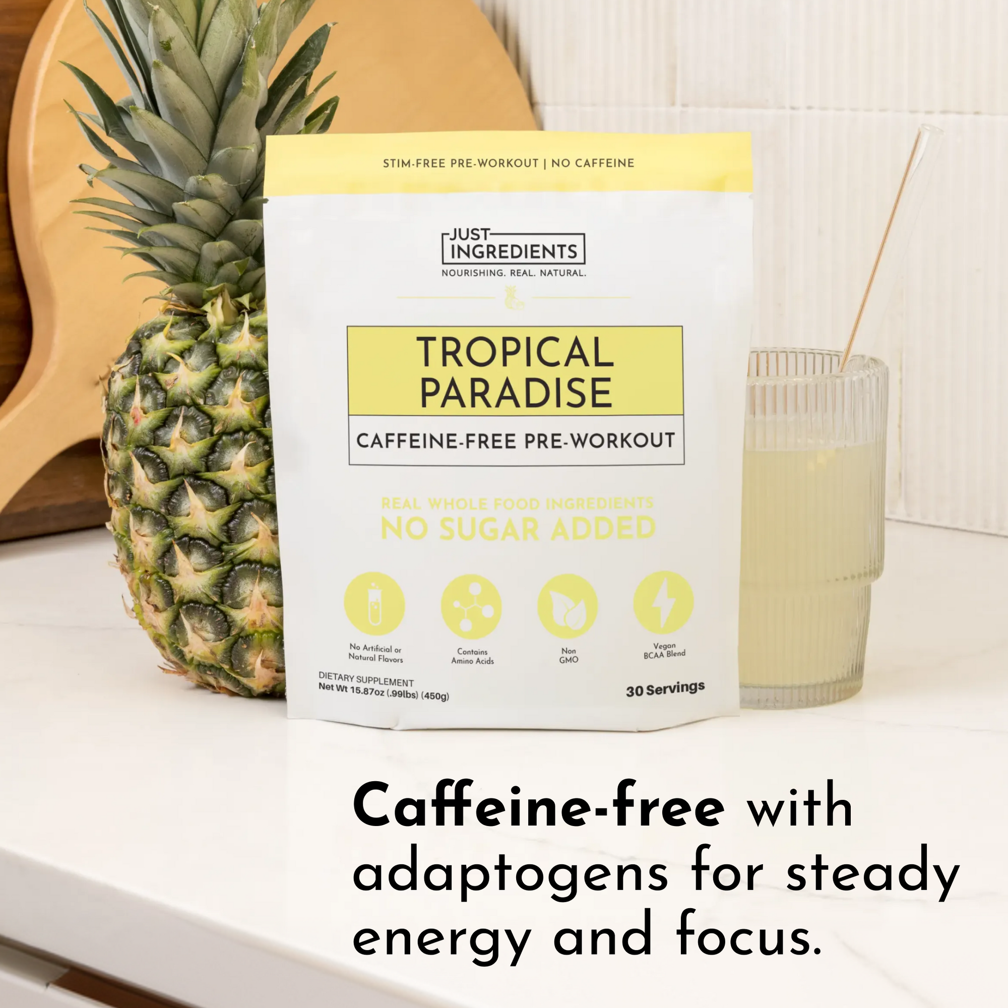 Caffeine-free pre-workout powder package next to a pineapple and a glass of light yellow drink on a countertop.