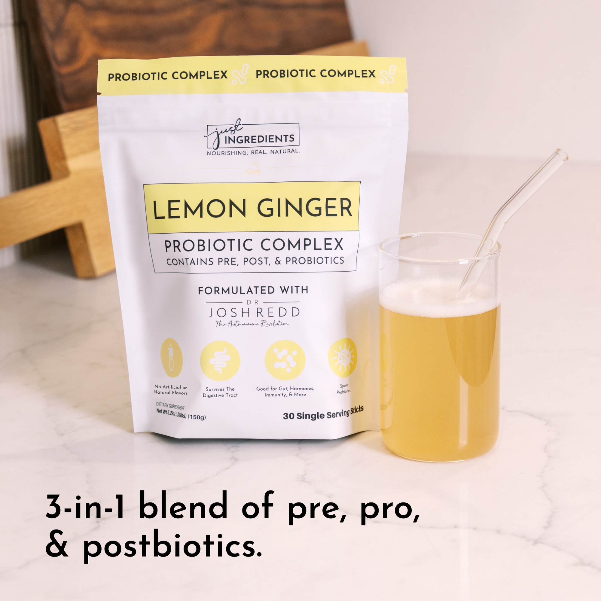 Pouch of Lemon Ginger Probiotic Complex next to a glass of light yellow liquid with a straw.