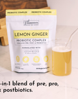 Pouch of Lemon Ginger Probiotic Complex next to a glass of light yellow liquid with a straw.