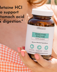 Brown glass bottle of digestive enzyme supplement with white label held in hand with pink nail polish.