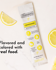 Lemonade electrolytes stick next to lemon slices on a marble surface, featuring product information on the packaging.