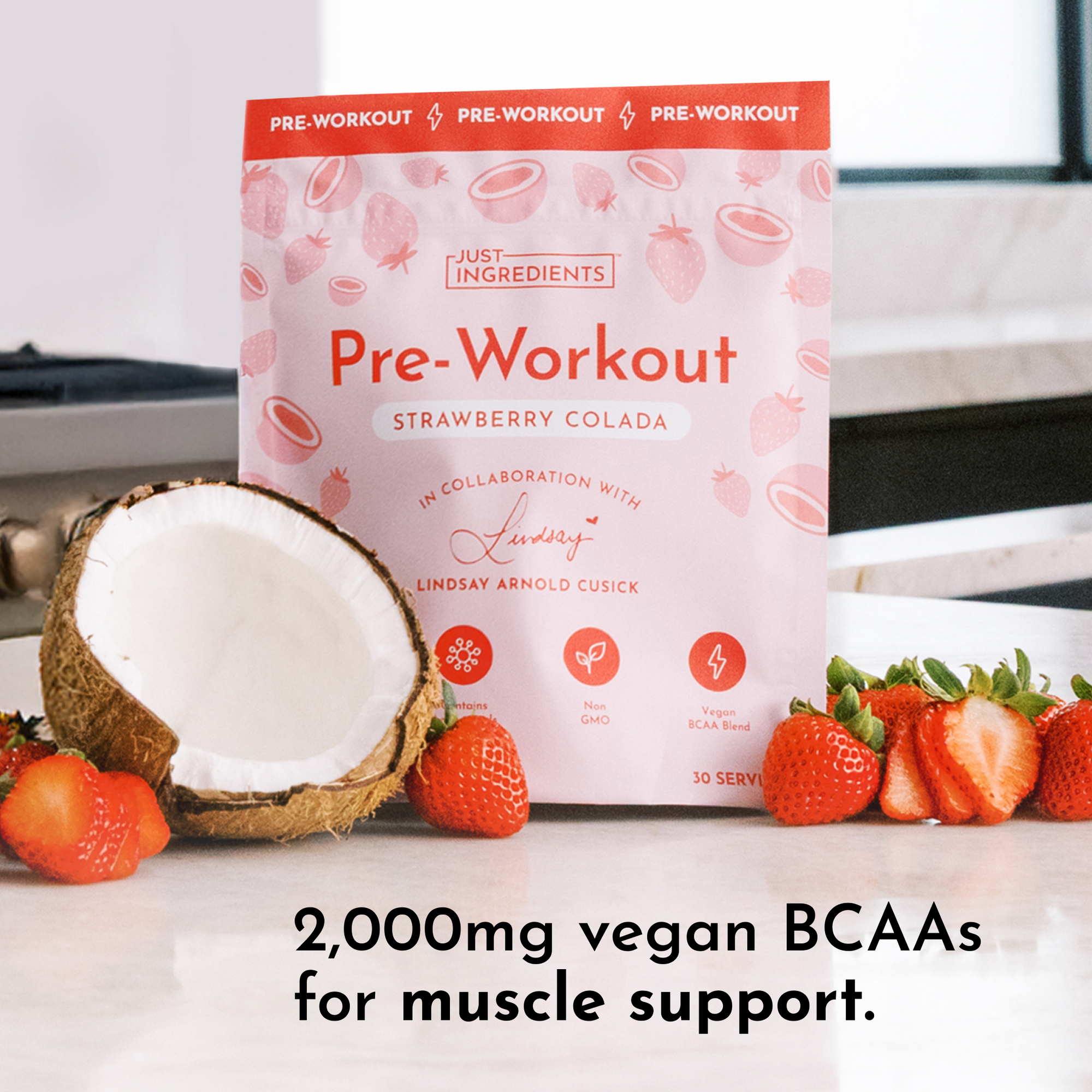 Pink packaging of Strawberry Colada Pre-Workout with coconut and strawberries on a countertop.