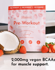 Pink packaging of Strawberry Colada Pre-Workout with coconut and strawberries on a countertop.