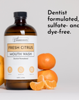 Brown glass bottle of Fresh Citrus mouth wash with citrus fruits beside it, labeled as dentist formulated and free from sulfa