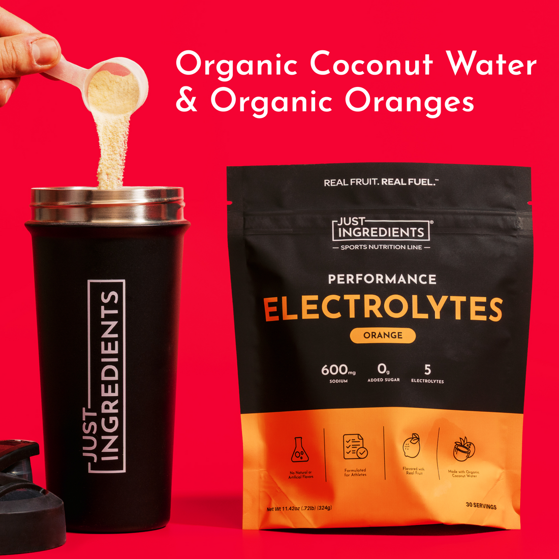 Spoon pouring orange electrolyte powder into a black tumbler beside the product pouch on a red background.
