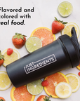 Black shaker bottle with "JUST INGREDIENTS" label surrounded by fresh strawberries, oranges, lemons, and limes.
