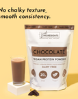 Chocolate vegan protein powder bag next to a glass of chocolate protein shake and a piece of dark chocolate.