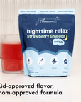 Dark blue pouch of strawberry limeade nighttime relax powder next to a glass filled with red liquid.