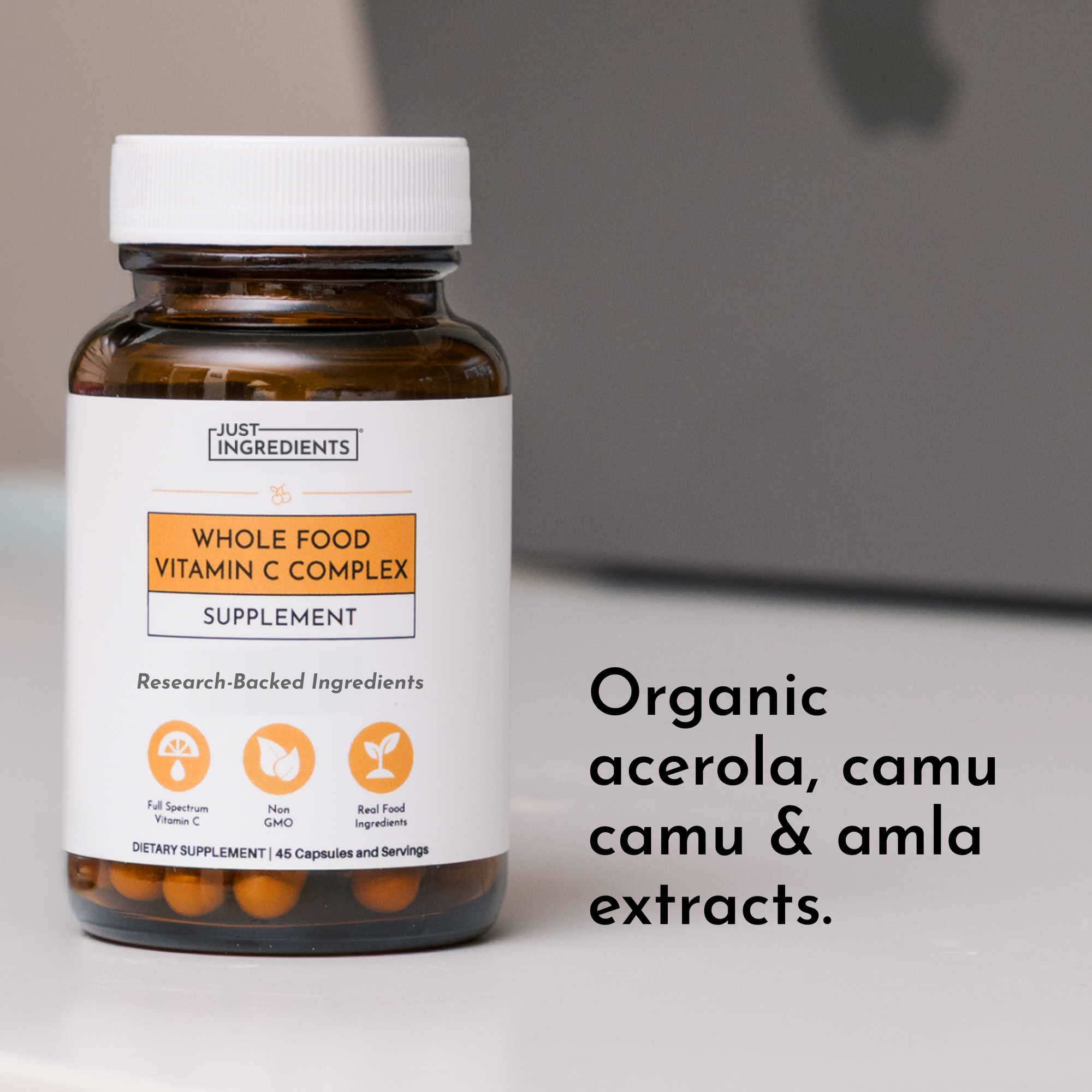Brown glass bottle with white cap containing orange capsules labeled "Whole Food Vitamin C Complex Supplement" by Just Ingred