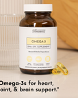 Brown glass bottle with white cap labeled "Omega-3 DHA + EPA Supplement" by Just Ingredients, with two yellow gel capsules be
