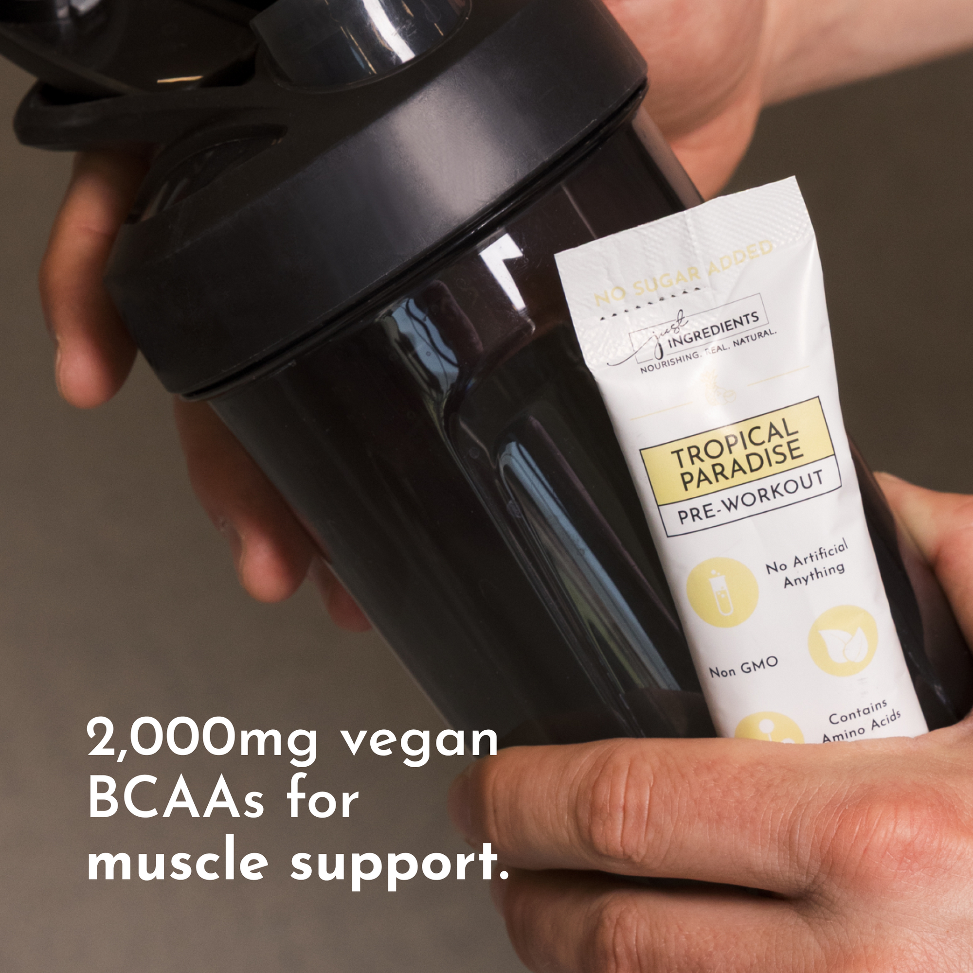 Hand holding a black shaker bottle with a Tropical Paradise Pre-Workout stick next to it.