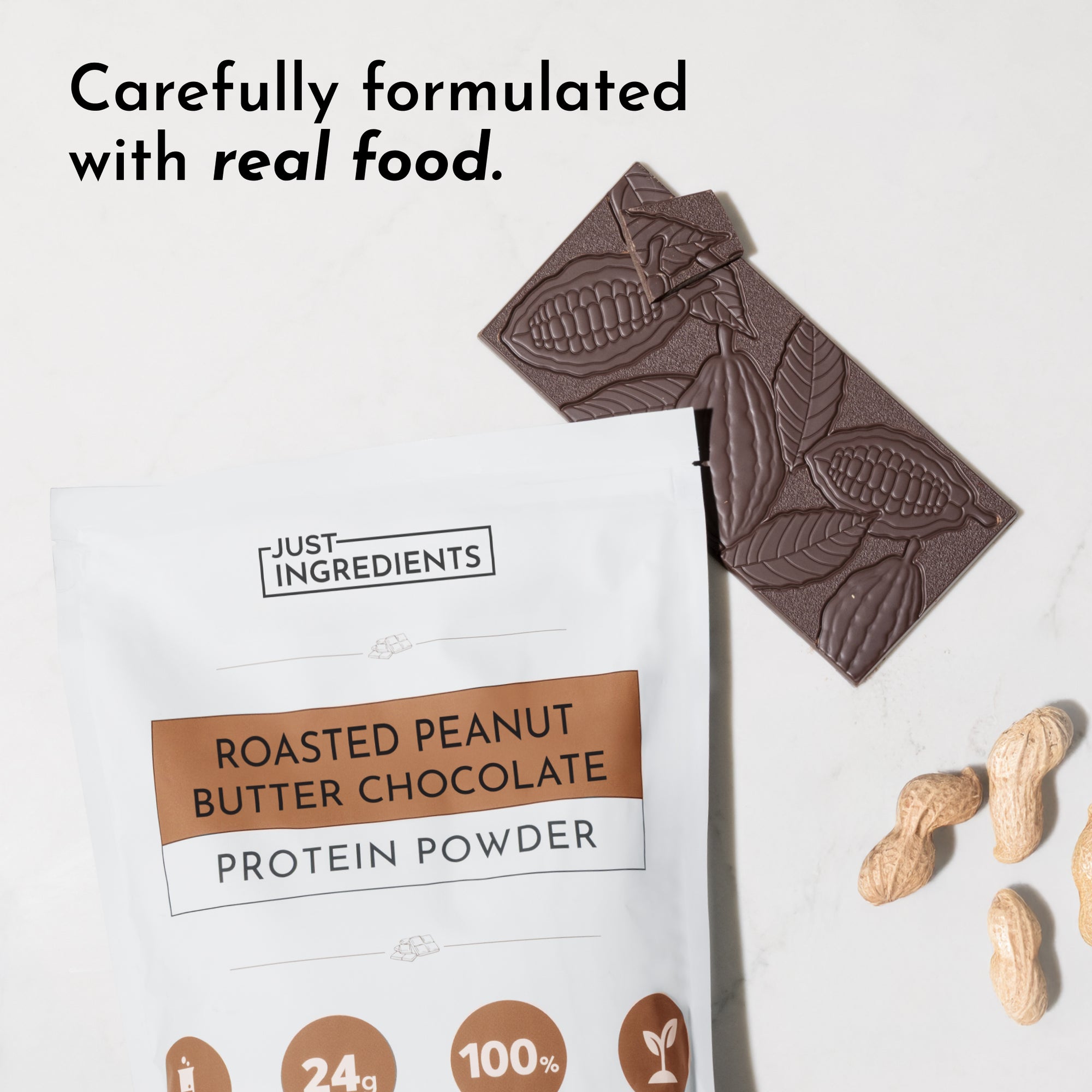 White pouch of roasted peanut butter chocolate protein powder next to chocolate bar and peanuts on a marble surface.