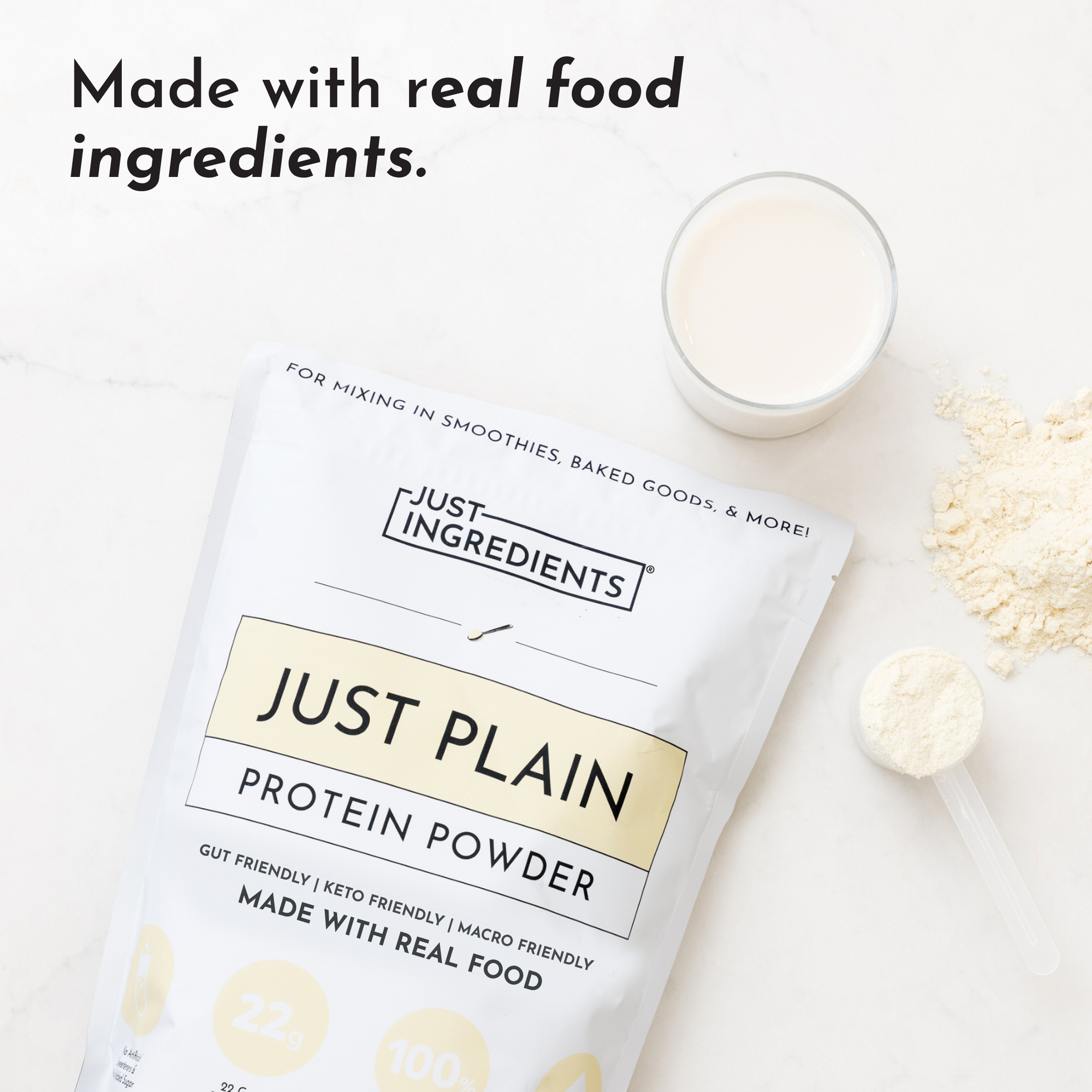 White protein powder package labeled "Just Plain" next to glass of mixed powder and measuring spoon on white surface.