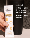 Hand holding an Orange Pineapple pre-workout stick next to a black container on a light surface.
