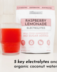 A glass of red raspberry lemonade next to a bag labeled "Raspberry Lemonade Electrolytes" with nutritional information.