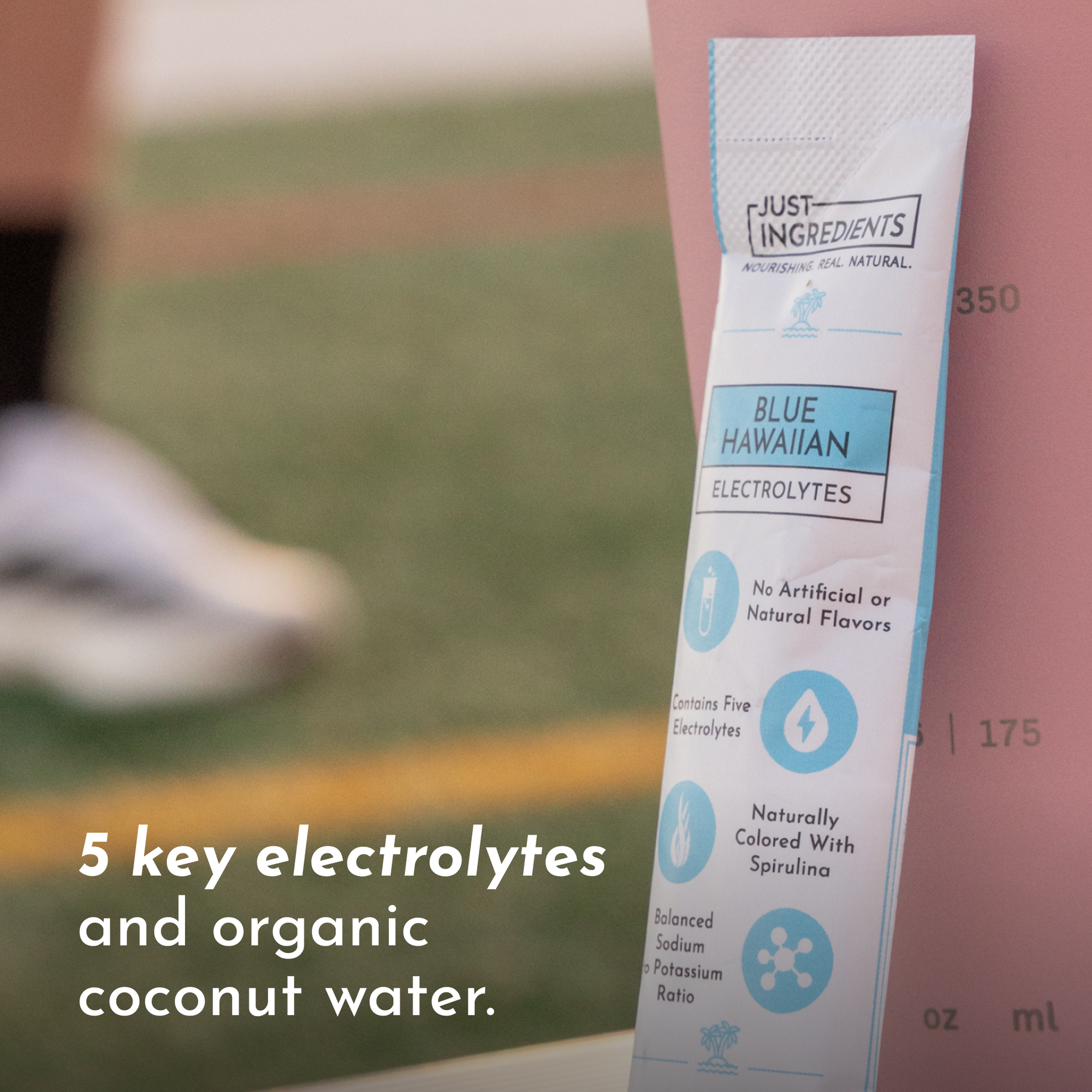 Electrolyte stick packet with blue design, listing ingredients and benefits, placed next to a measuring cup.