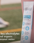 Electrolyte stick packet with blue design, listing ingredients and benefits, placed next to a measuring cup.