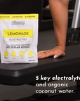 Lemonade Electrolytes package on a gym bench with a hand resting on it, featuring product details and serving information.