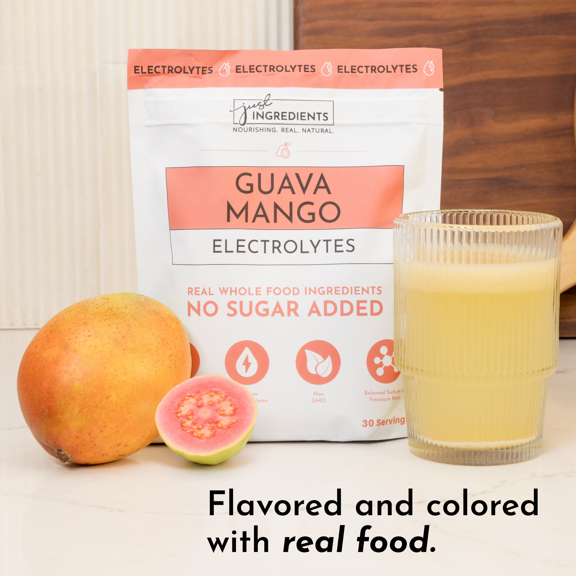 Pouch of Guava Mango Electrolytes next to a whole mango, a halved guava, and a glass of yellow liquid.