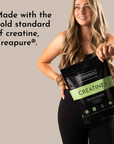 Woman holding a black pouch labeled "CREATINE+" with a green stripe, wearing a black outfit against a neutral background.
