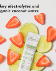 Electrolyte stick surrounded by sliced strawberries and lime, featuring a green and silver packaging.