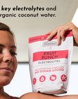 A person holds a bag of Fruit Punch Electrolytes featuring a red and white design with text about its ingredients.