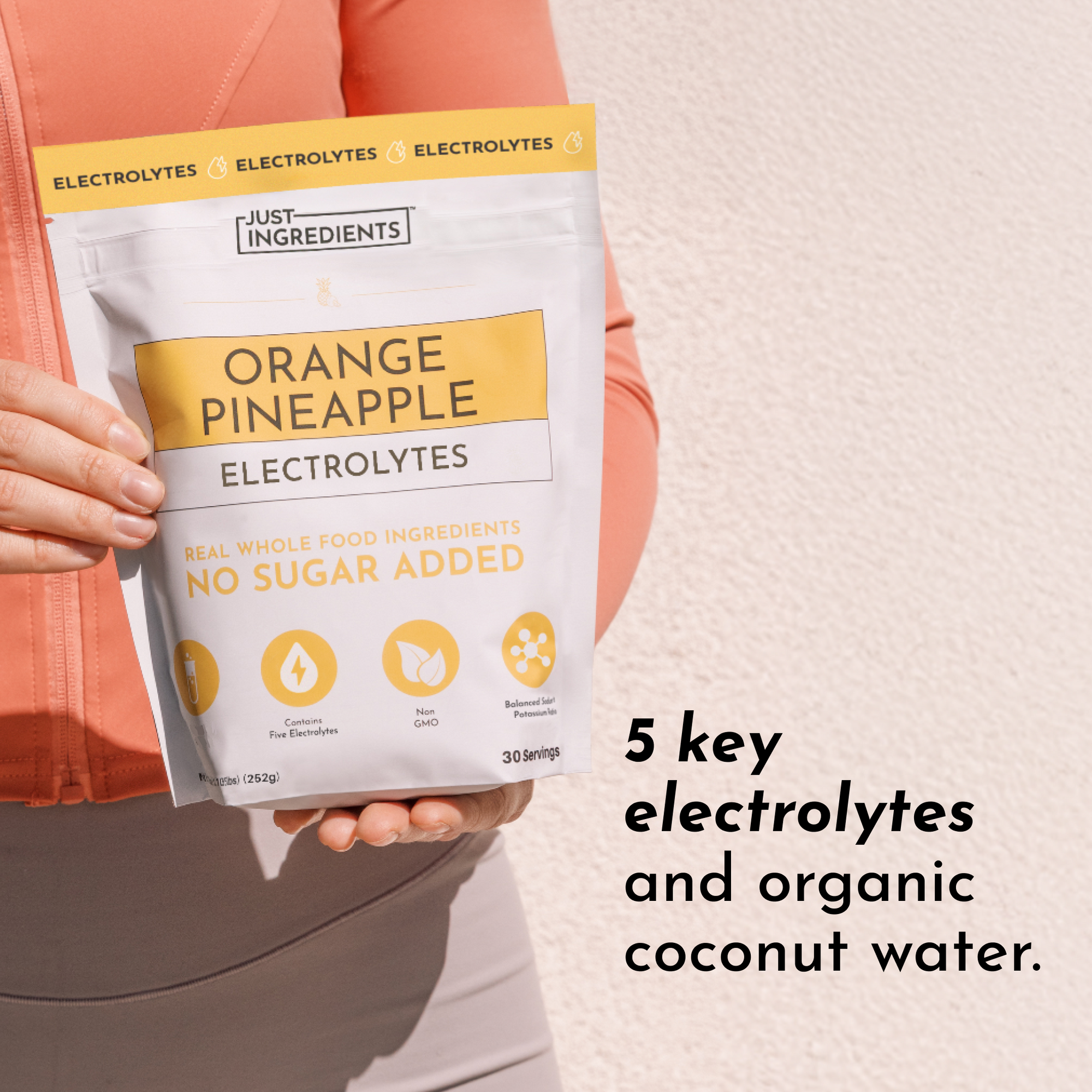 A person holds a pouch of Orange Pineapple Electrolytes with a white and yellow design, featuring text about its ingredients.