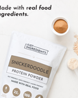 Snickerdoodle protein powder pouch with cinnamon powder in white bowl and measuring scoops on white surface.