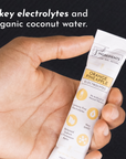 Hand holding a stick packet labeled "Orange Pineapple Electrolytes" with nutritional information visible.