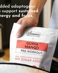 Hand holding white packet labeled "Guava Mango Pre-Workout" with red accent stripe and "Just Ingredients" branding.