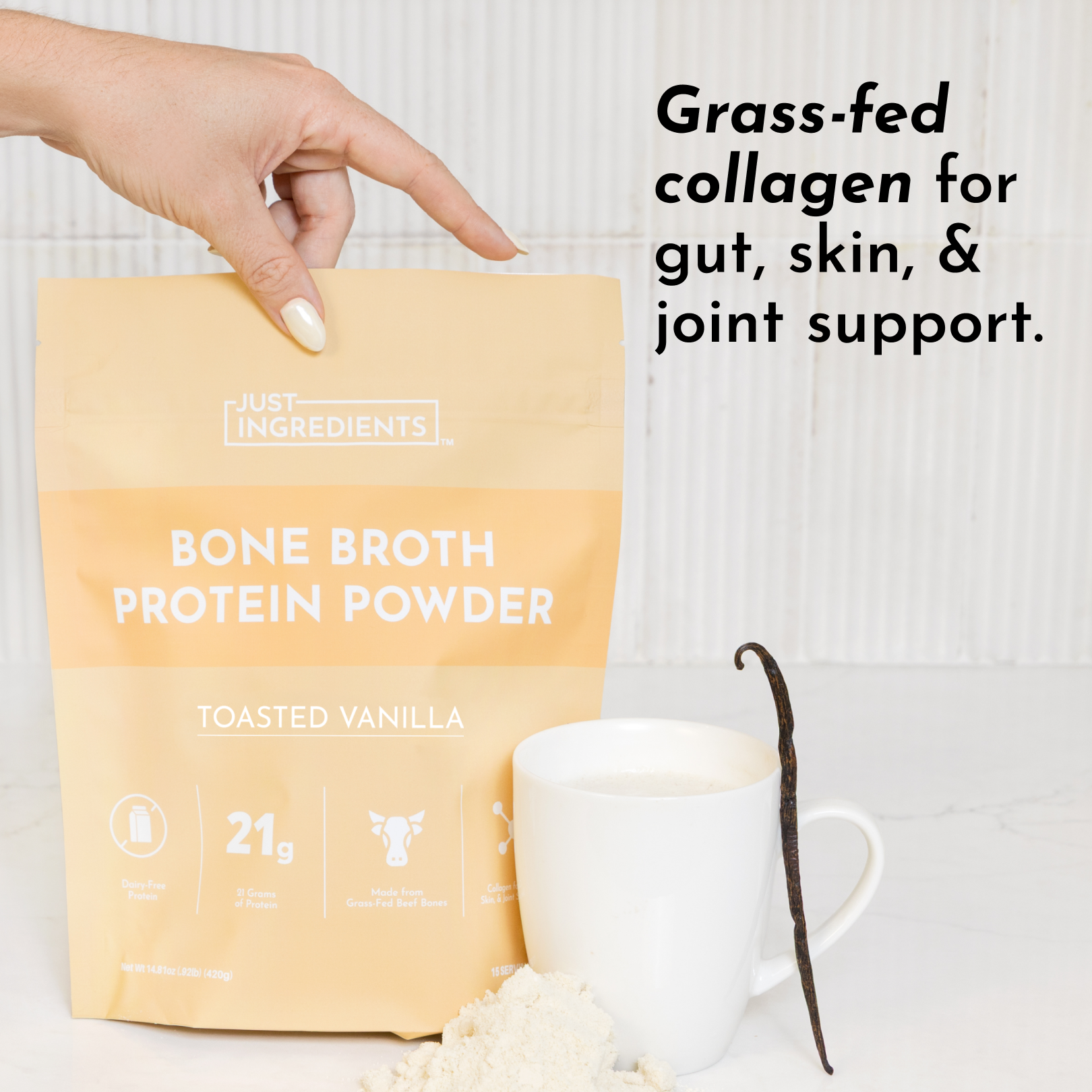 A hand holds a yellow pouch of bone broth protein powder next to a cup of liquid and a vanilla bean.