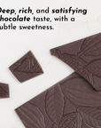 Dark chocolate pieces with leaf and cocoa pod designs on a white surface.