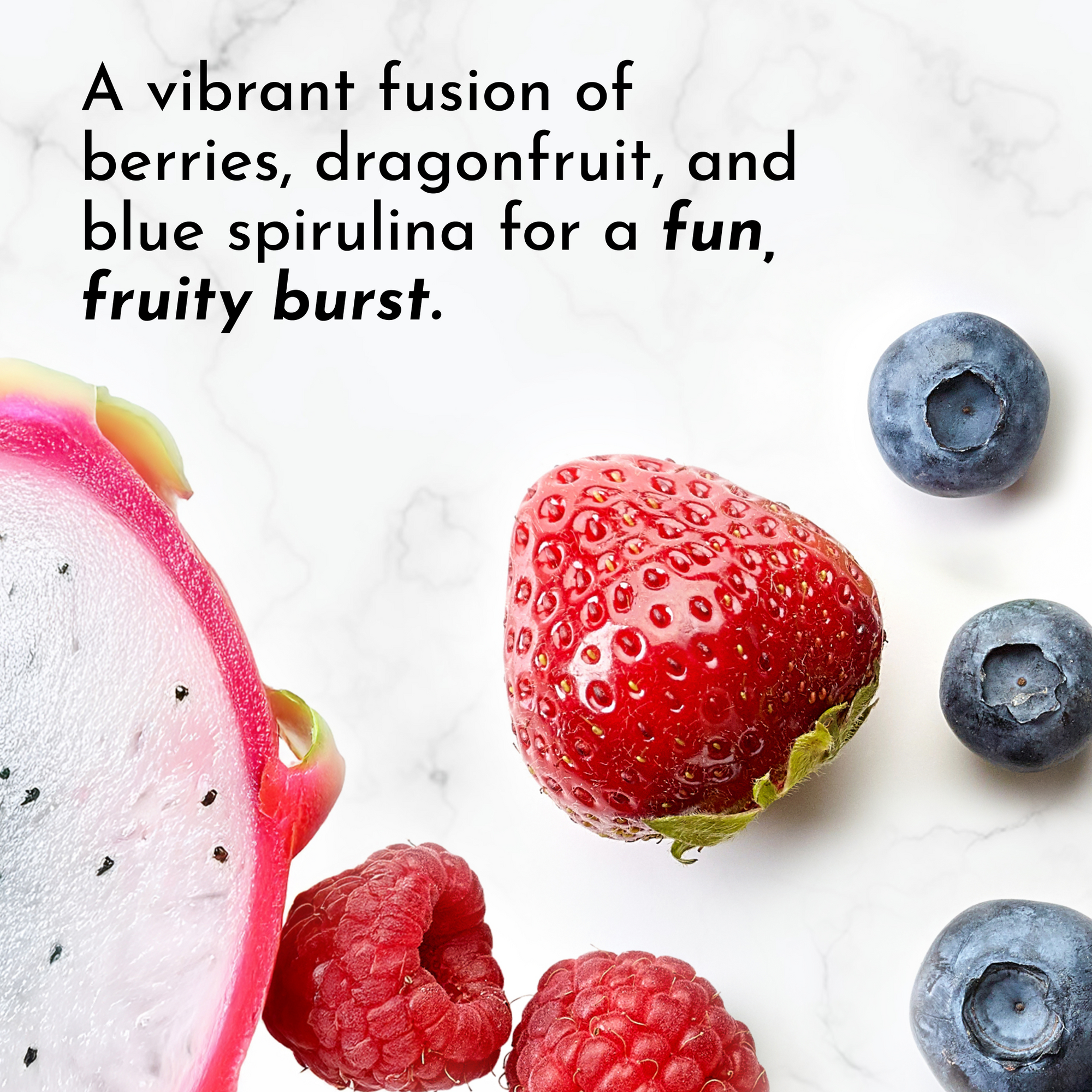 Sliced dragonfruit, a strawberry, raspberries, and blueberries arranged on a light marble background.