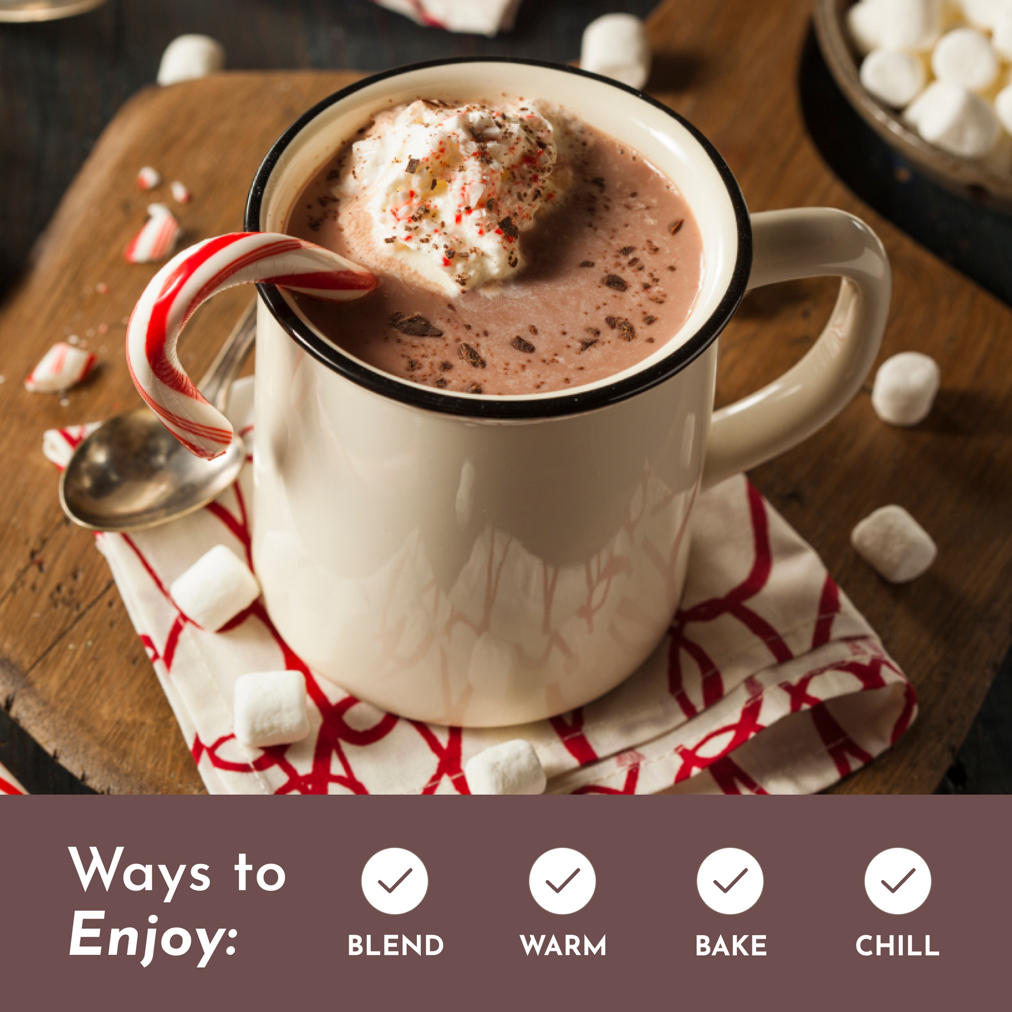 Mug of hot chocolate topped with whipped cream and a candy cane, surrounded by marshmallows on a wooden surface.