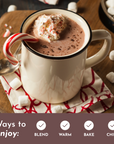 Mug of hot chocolate topped with whipped cream and a candy cane, surrounded by marshmallows on a wooden surface.
