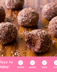 Chocolate protein balls coated in shredded coconut on a wooden surface.