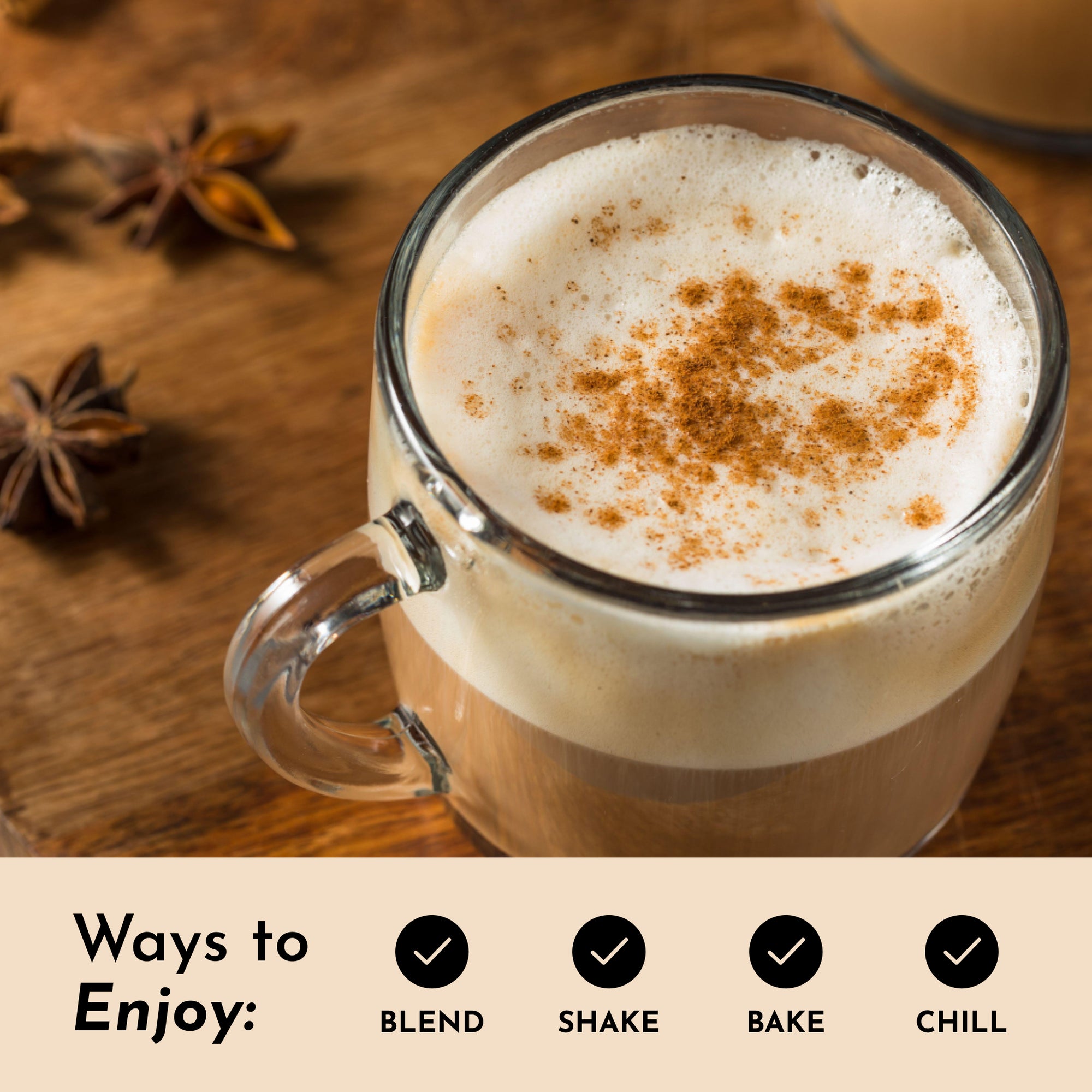 A glass mug filled with frothy chai beverage topped with a sprinkle of spice, placed on a wooden surface.