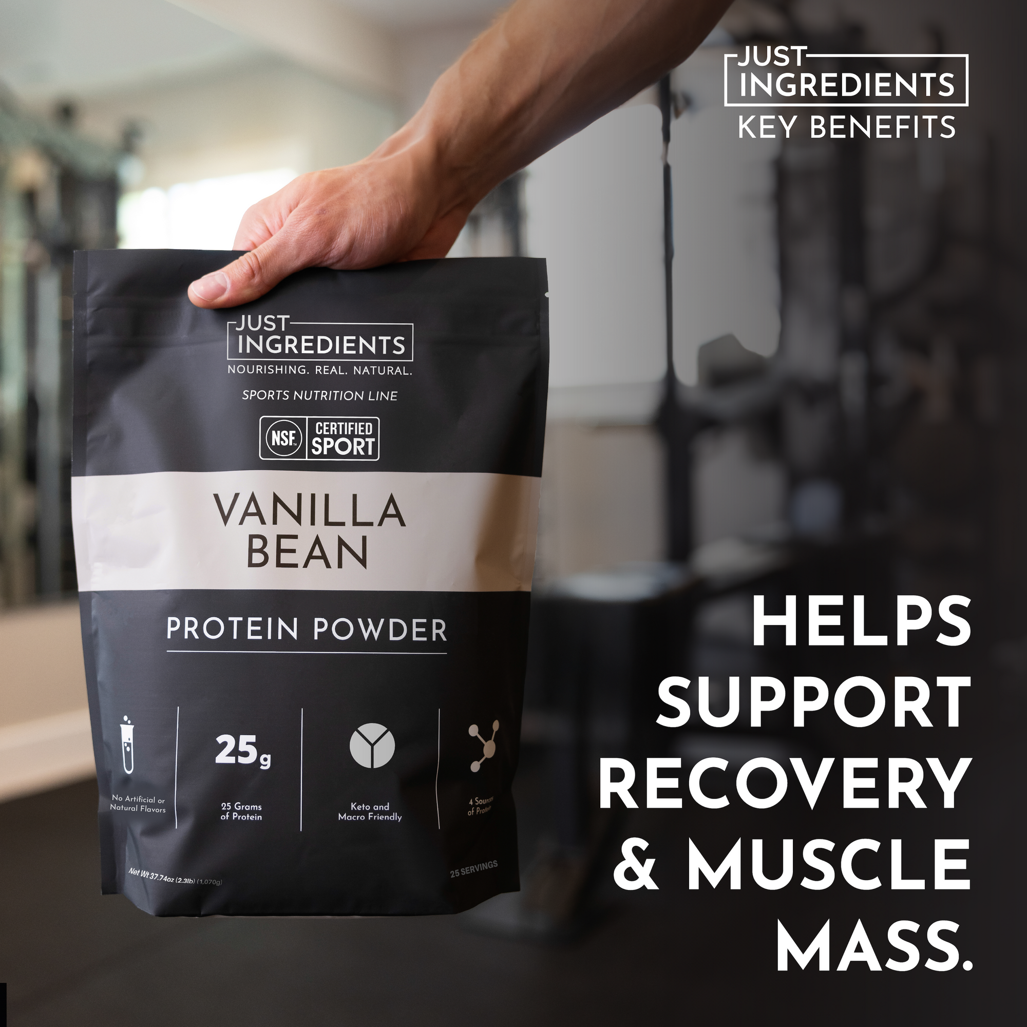Black and white bag of Vanilla Bean Protein Powder held in a hand, with gym equipment blurred in the background.