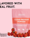 Pink packaging of clear protein powder labeled "Strawberry Slush" with fresh strawberries in front.