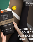 Black protein powder bag labeled "Snickerdoodle" held by a person, with a paddle and ball in the background.