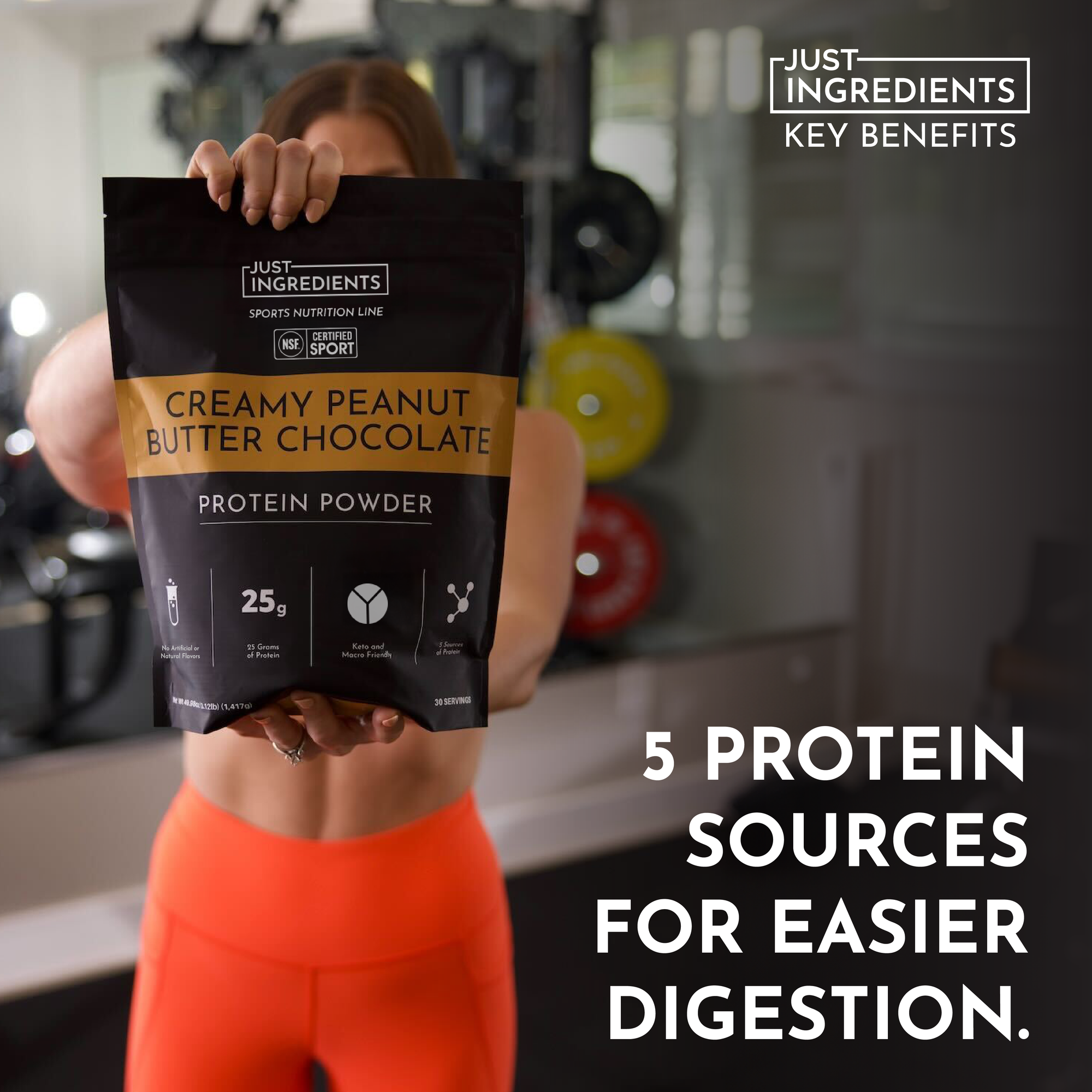 A person holds a bag of creamy peanut butter chocolate protein powder in a gym setting.