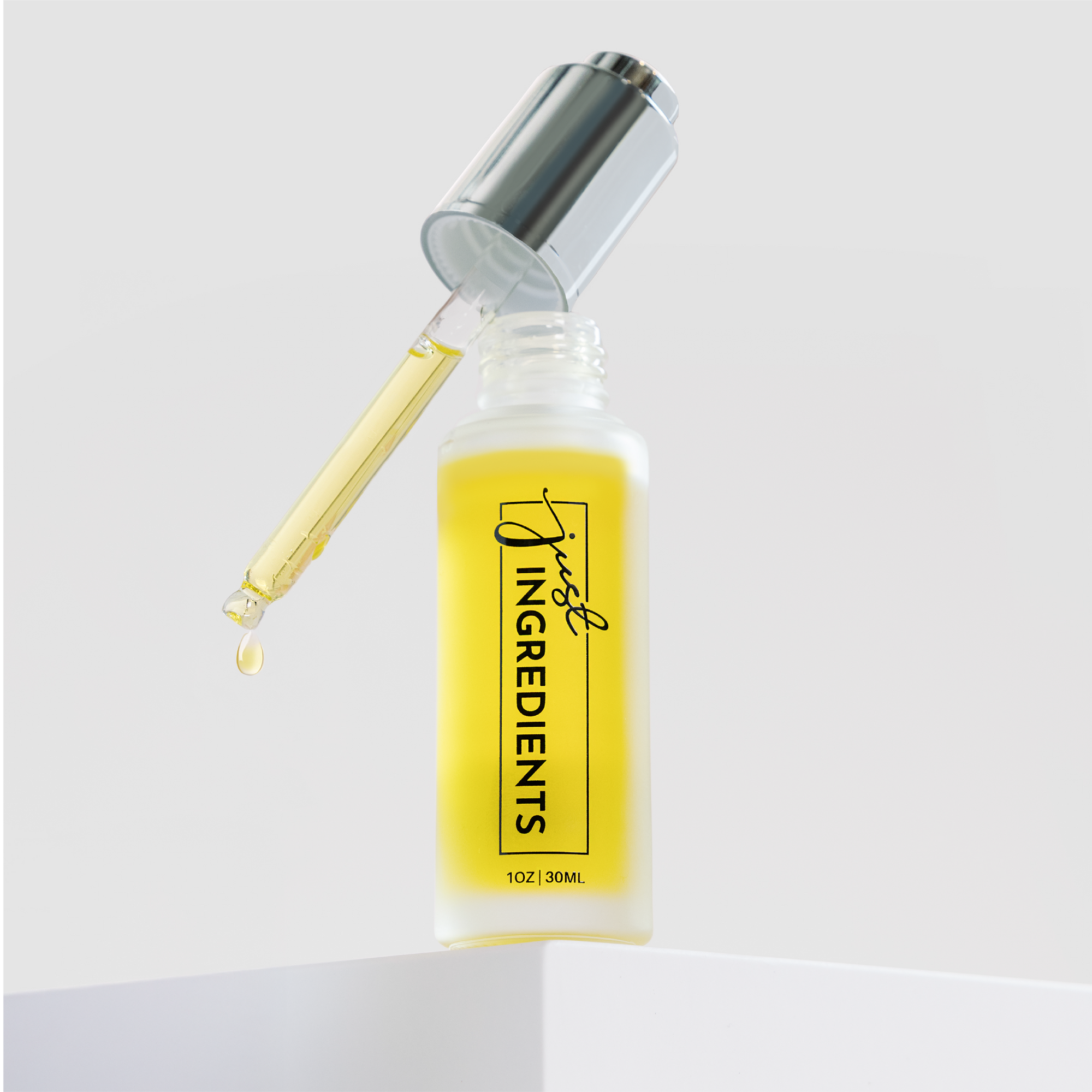 Glass dropper bottle with yellow face serum and silver cap, labeled "Just Ingredients," on a white surface.