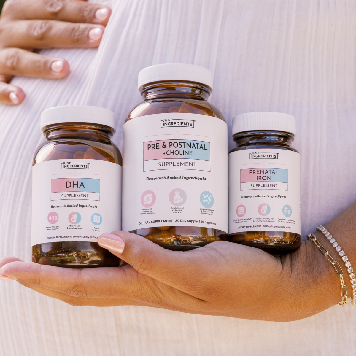 Three amber supplement bottles labeled DHA, Pre &amp; Postnatal + Choline, and Prenatal Iron held in a hand.