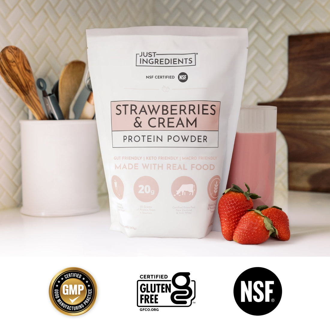 Glass of pink strawberries & cream shake next to a pouch of the protein powder on a countertop.