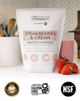 Glass of pink strawberries & cream shake next to a pouch of the protein powder on a countertop.