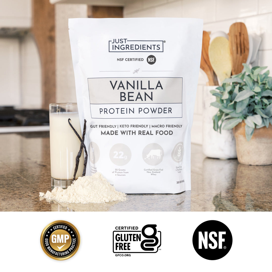 White bag of Vanilla Bean Protein Powder with a scoop and a glass of protein shake on a countertop.