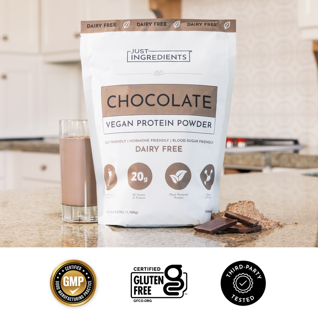 Hand holding a clear scoop of beige protein powder above a glass with a chocolate shake and chocolate pieces behind.